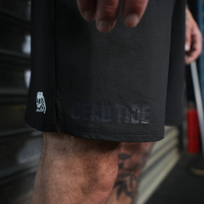 Black shorts with a Dead Tide logo on a person's leg, blurred background