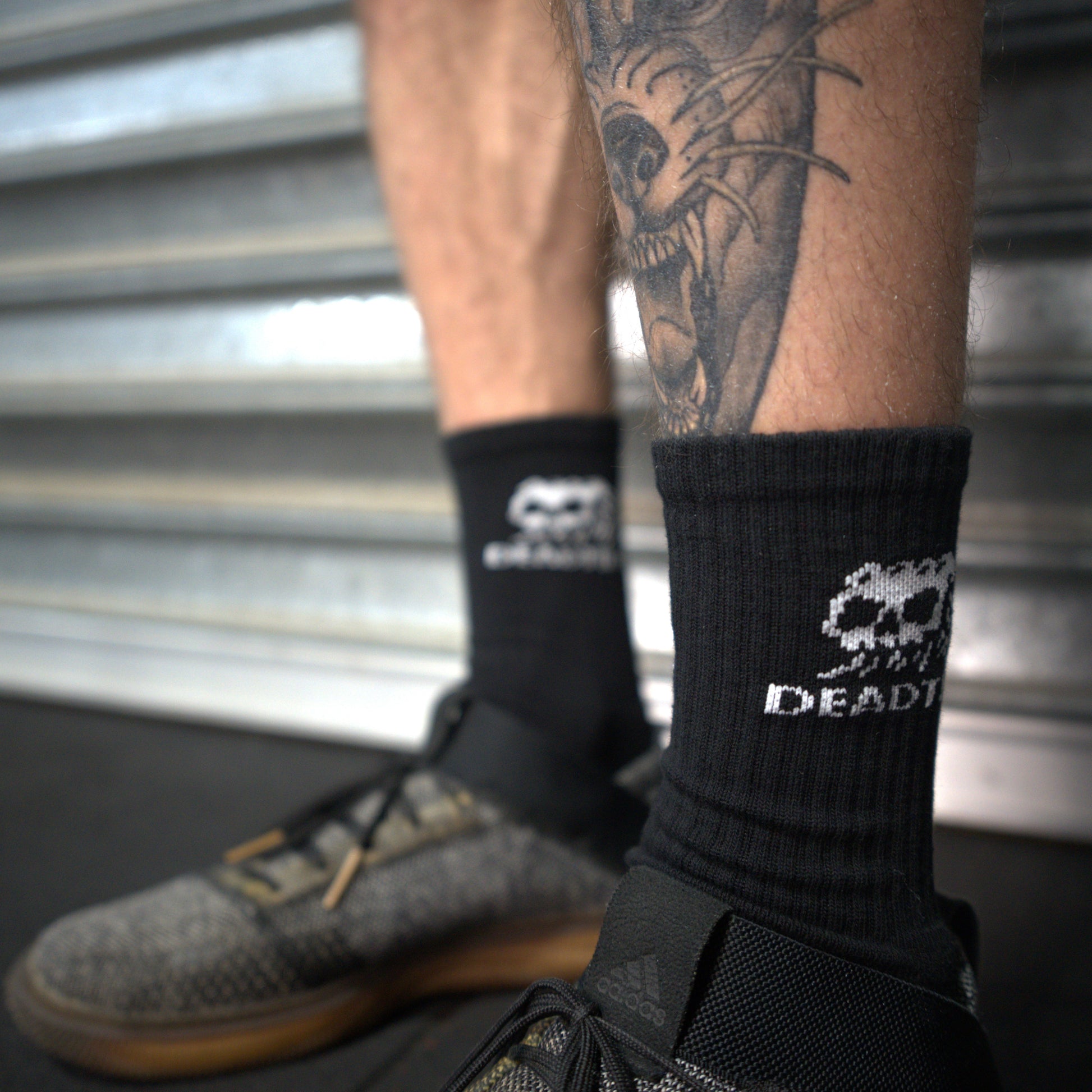 Black socks with skull logo design worn by a person with tattoos.