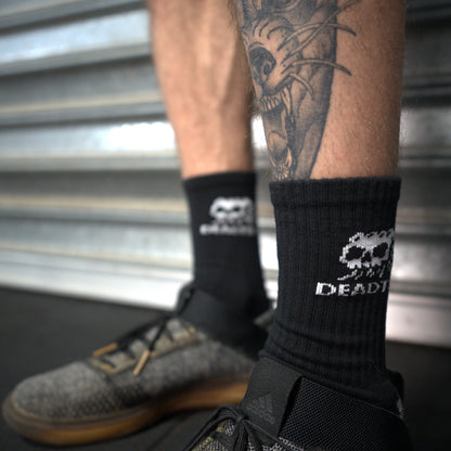 Black socks with skull logo design worn by a person with tattoos.